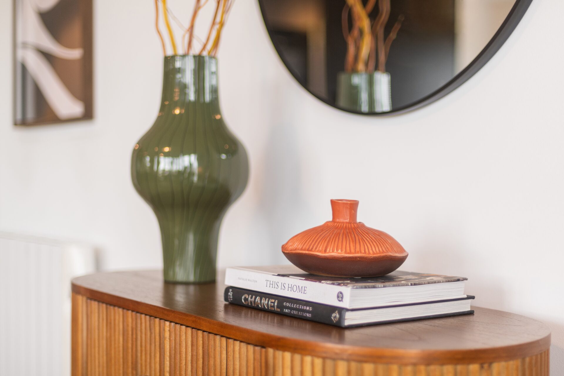 Styled sideboard in an EirStay Dublin serviced apartment — green vase, design books and a round mirror reflecting warm interior details