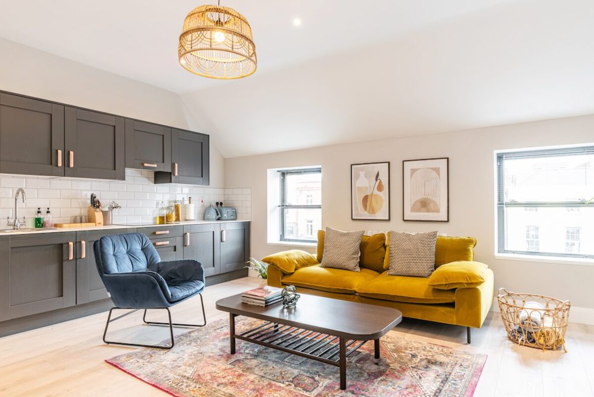 Open plan living room with mustard velvet sofa and dark grey kitchen in EirStay corporate short stay apartment Camden Street Dublin 2