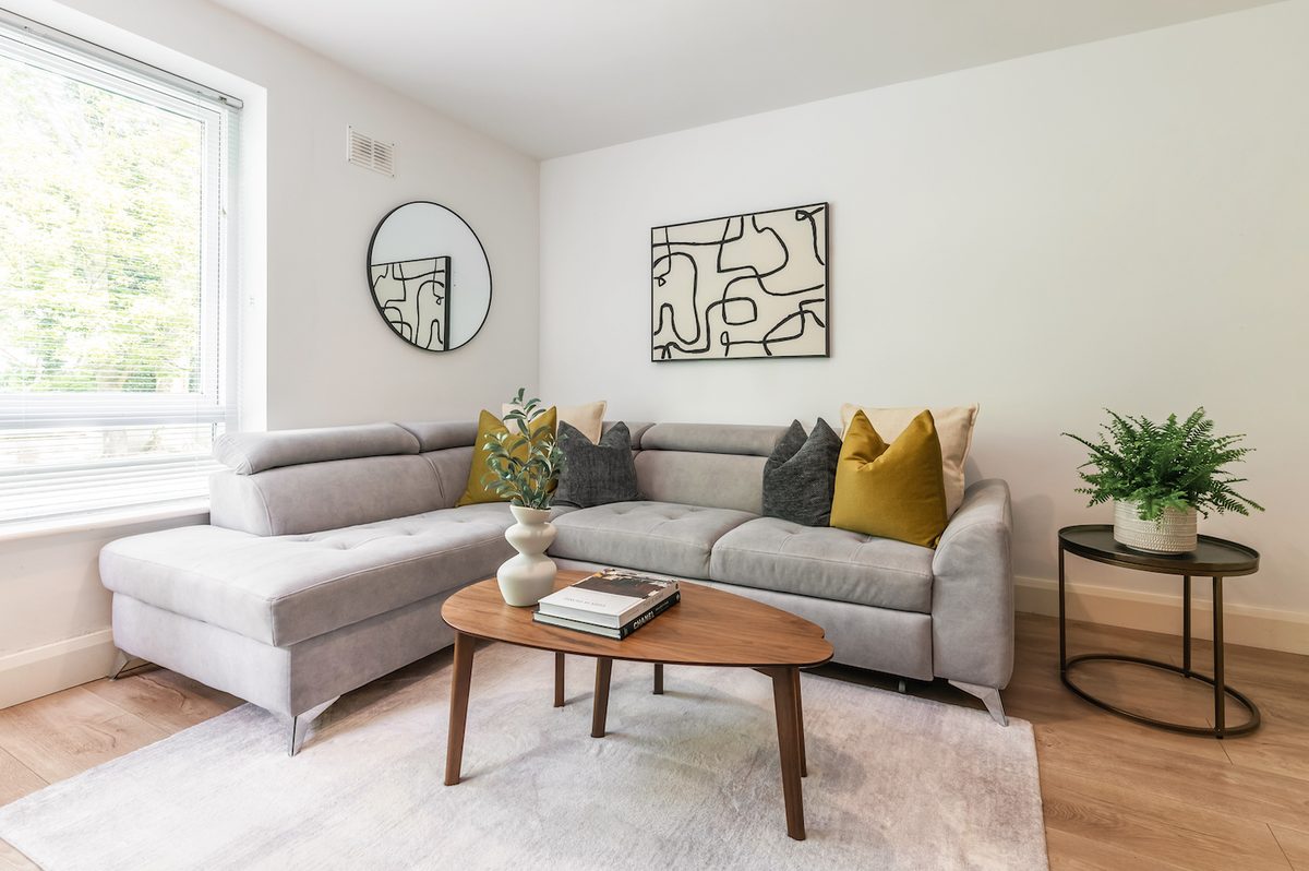 Light-filled living room with corner sofa, round mirror and house plants in EirStay Islandbridge one-bedroom apartment Dublin 8
