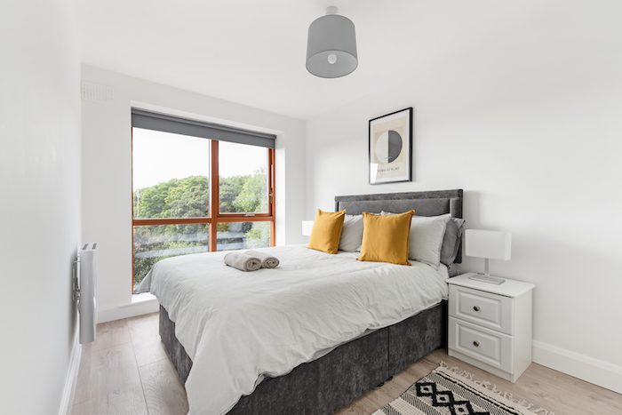 King-size bedroom with mustard cushions Hilma af Klint print and floor-to-ceiling window with tree views in EirStay corporate accommodation Kilmainham Dublin 8