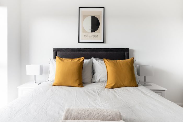 King bed with charcoal upholstered headboard mustard cushions and Hilma af Klint art print in EirStay corporate short stay Kilmainham Dublin 8